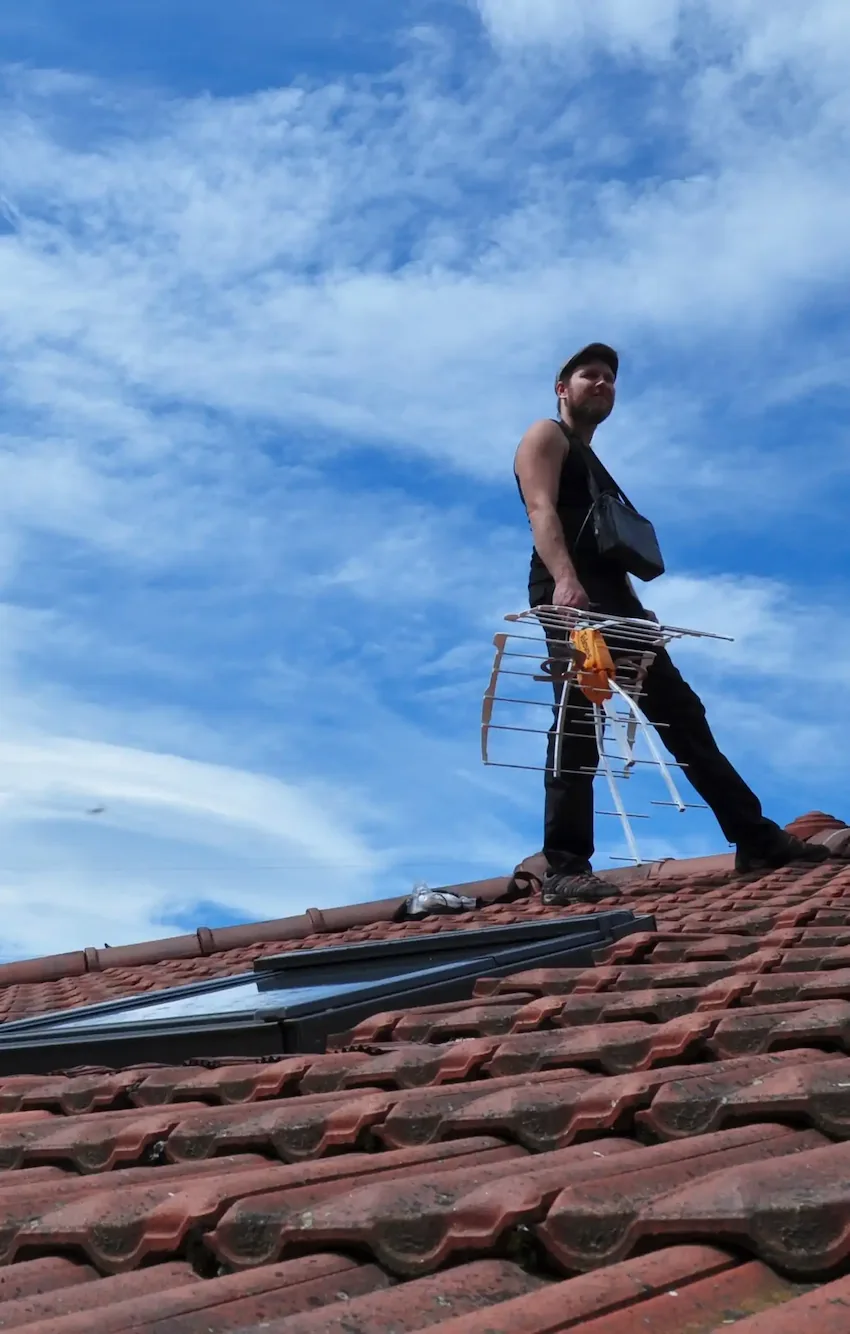 Antenniste qui installe une antenne râteau sur le toit d'une maison