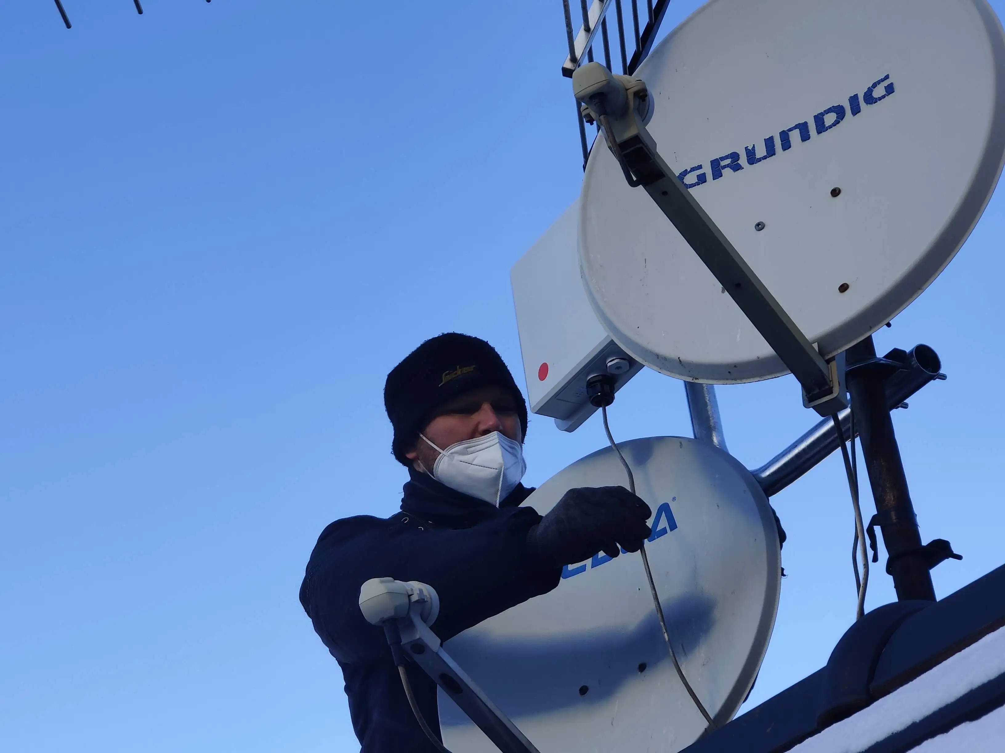 Artisan antenniste masqué installant plusieurs antennes paraboliques et râteaux sur un toit