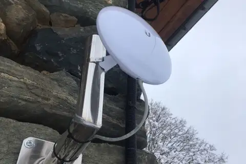 Antenne internet wifi Alsatis blanche et ronde fixée sur le mur en pierre d'une maison
