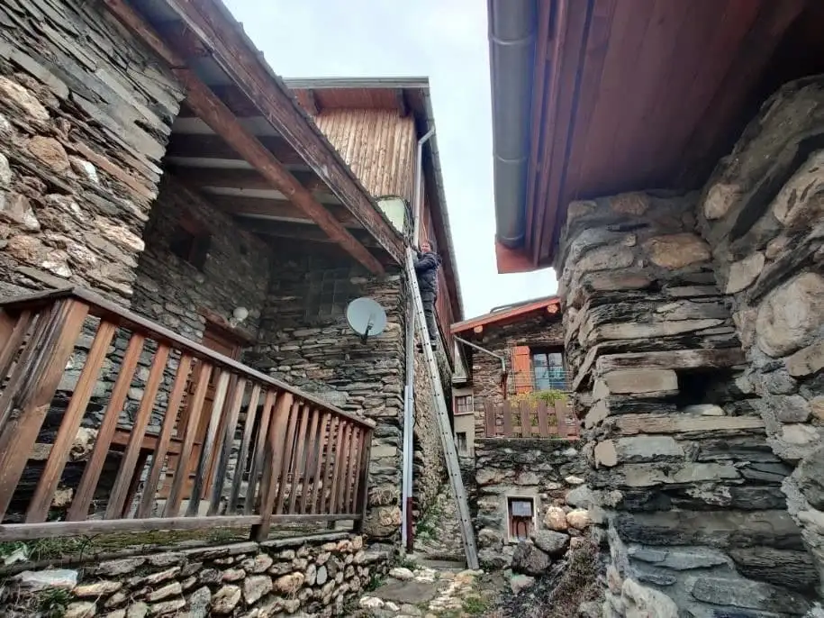 Artisan antenniste en haut d'une échelle sur une maison en pierre