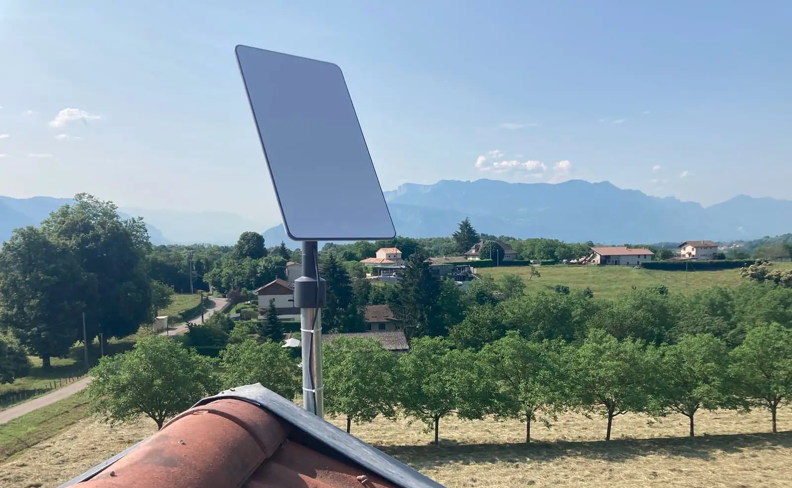 Antenne Starlink fixée sur un toit avec des arbres en contrebas et la montagne au loin