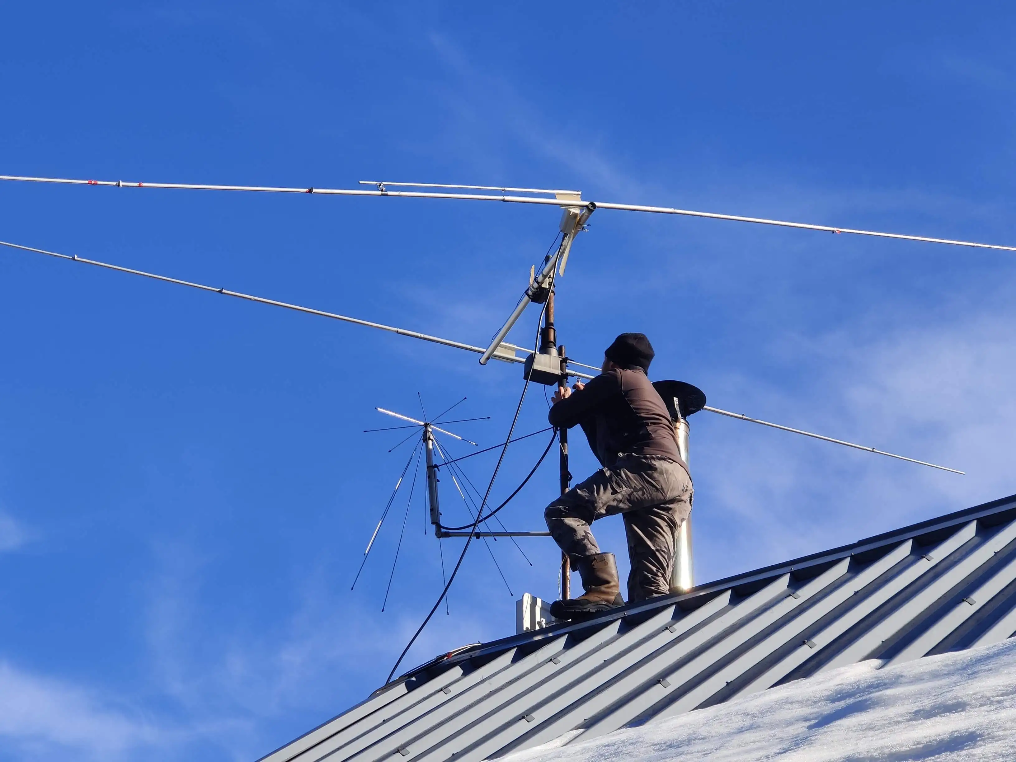 Artisan antenniste installant plusieurs antennes sur un toit en tôle enneigé vue rapprochée