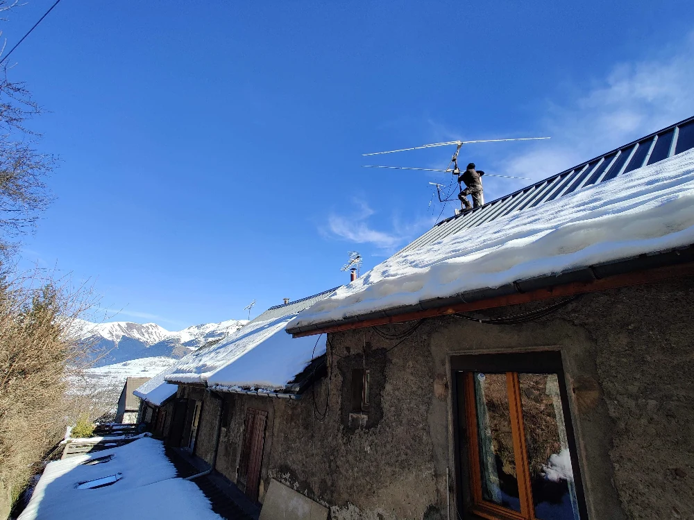 Artisan antenniste installant plusieurs antennes sur un toit en tôle enneigé vue éloignée