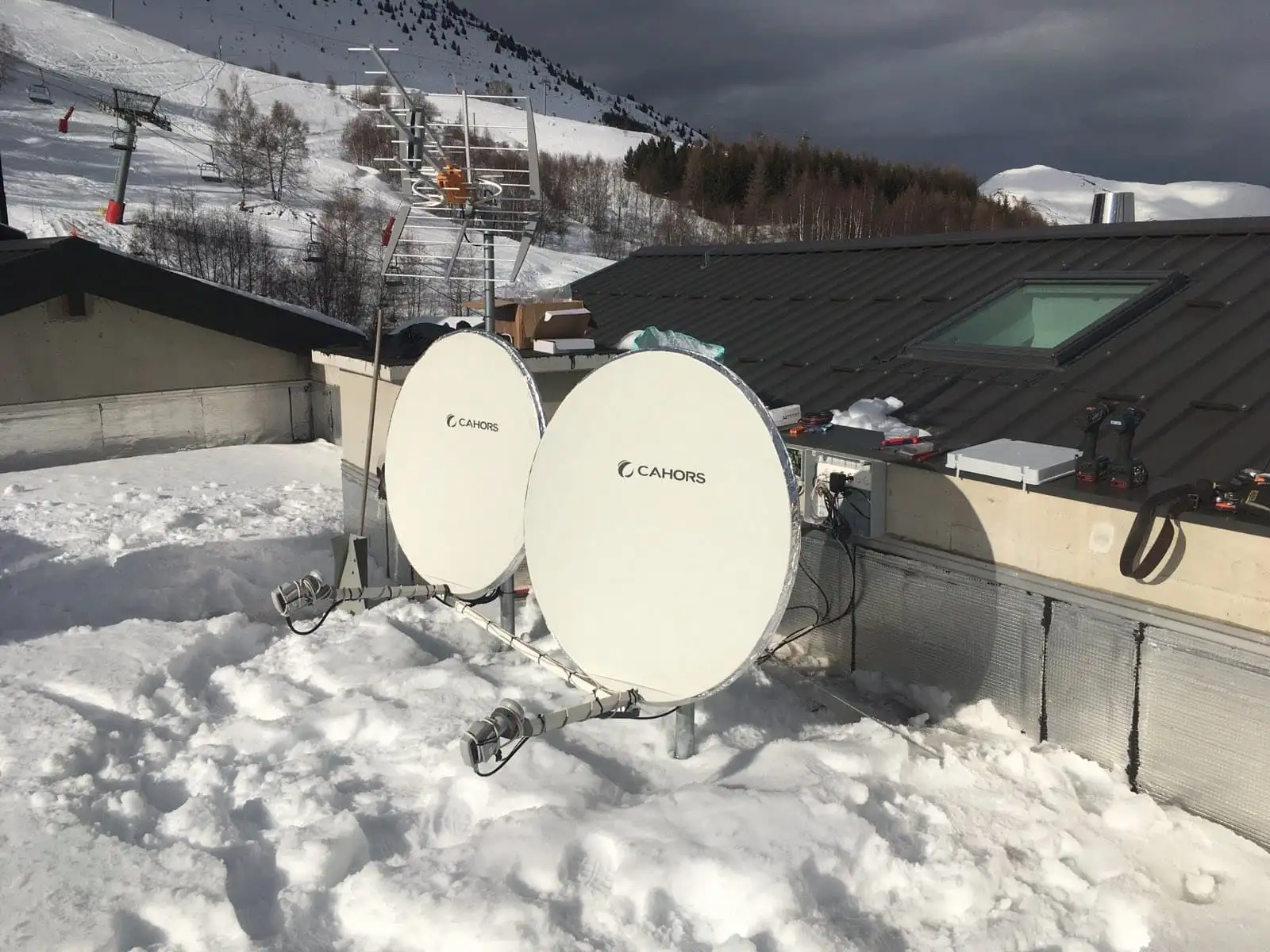 Deux paraboles et une antenne râteau installées sur un toit enneigé